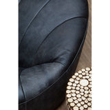 A round side table made of fir wood with a mosaic disc design, featuring a natural wood finish and a textured surface. The table is positioned next to a plush, dark-colored chair, showcasing its elegant and modern aesthetic. The background includes a soft, neutral-toned carpet
