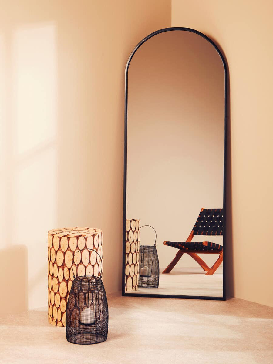 Lacuna Fir Wood Mosaic Disc Side Table and Stool featuring a circular design with a natural wood finish, positioned next to a black and red folding chair, reflecting light from a large arched mirror on a softly lit wall