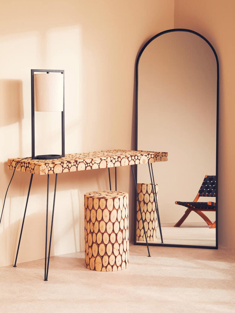 Lacuna Fir Wood Mosaic Disc Side Table and Stool featuring a circular mosaic design in natural wood tones, positioned next to a tall, arched mirror and a minimalist black chair against a soft beige wall. The table has a sturdy, textured surface and complements the overall warm aesthetic of the room