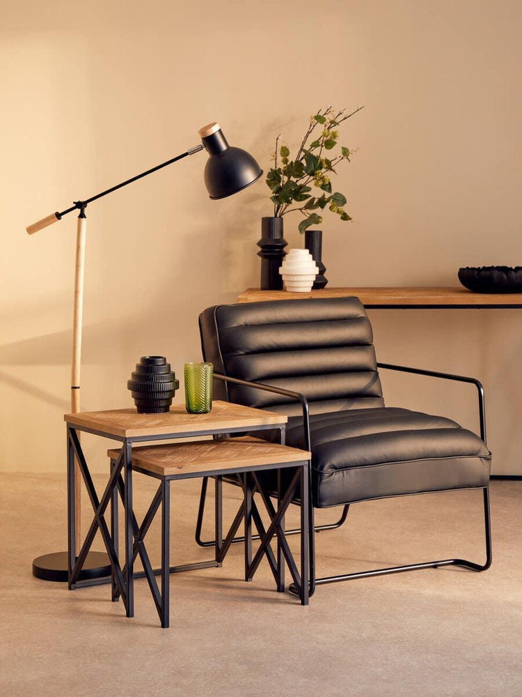 Black leather armchair with metal frame beside nested wood tables and floor lamp
