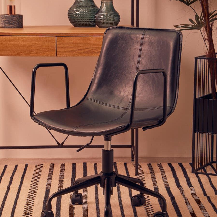 Black leather office chair with metal arms on castor wheels beside wooden desk
