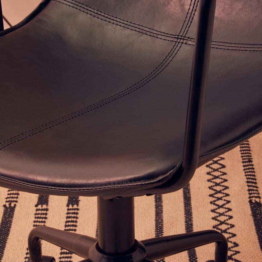 Black leather office chair seat with stitching detail and metal legs on patterned rug