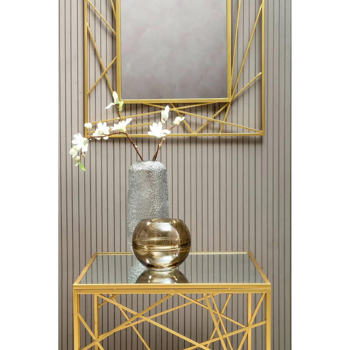 Gold geometric console table with glass top, decorative vases, and matching wall mirror