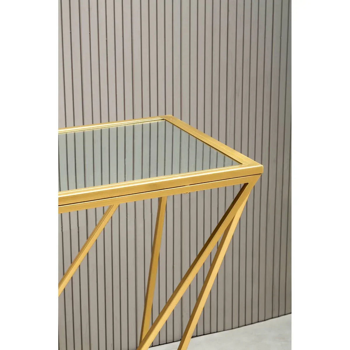 Gold metal and glass side table with geometric legs against a slatted wall