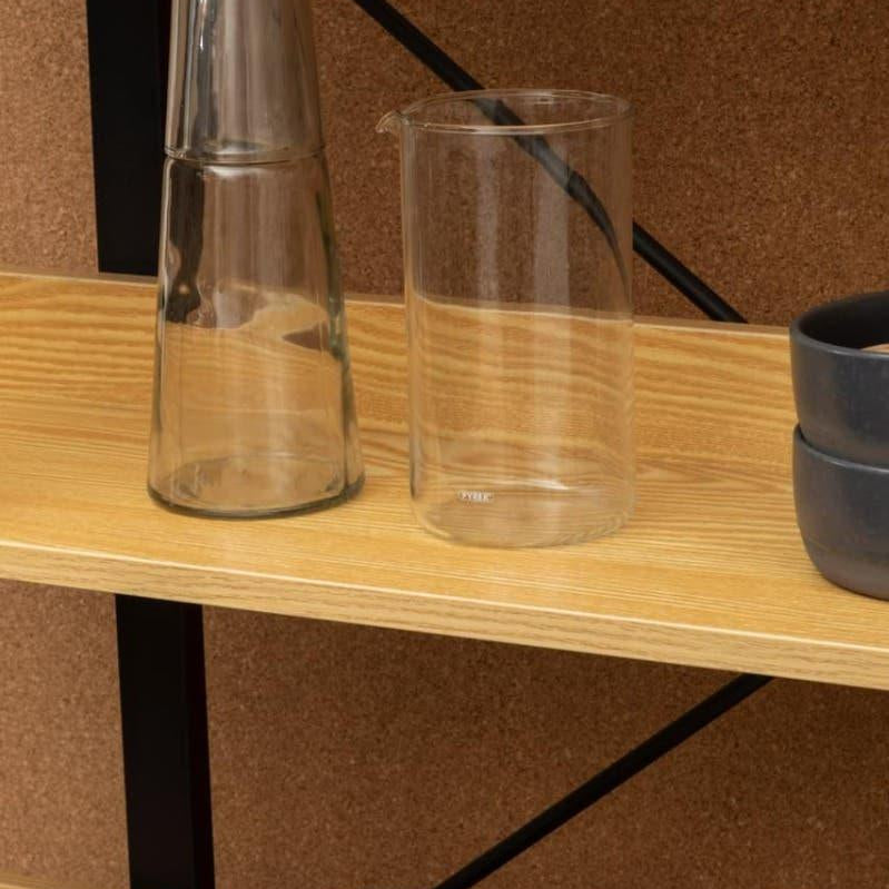 Wooden shelving unit with glass carafe, glass jug, stacked black bowls and metal funnel