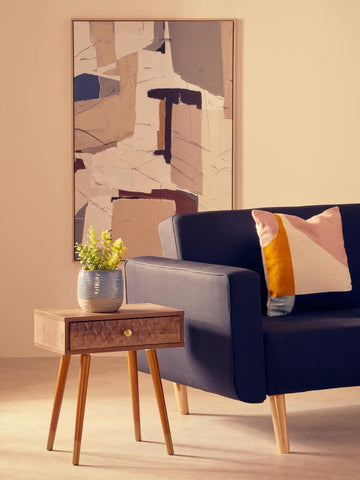 Wooden side table with drawer and plant beside navy fabric sofa and modern abstract art