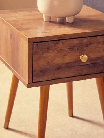 Wooden bedside table with gold knob and tapered legs on tile floor
