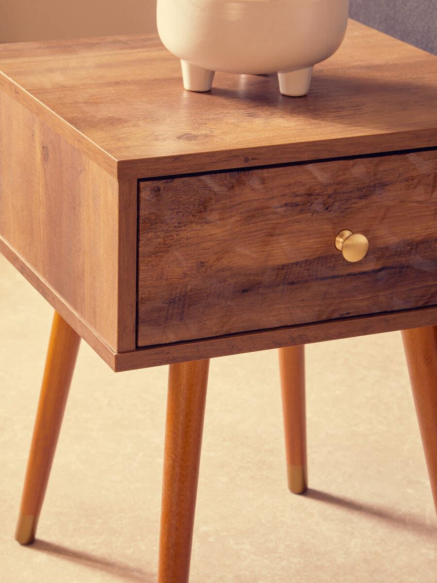 Wooden bedside table with gold knob and tapered legs on tile floor