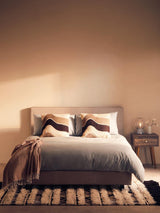 Modern upholstered bed with grey bedding, patterned pillows, and bedside table