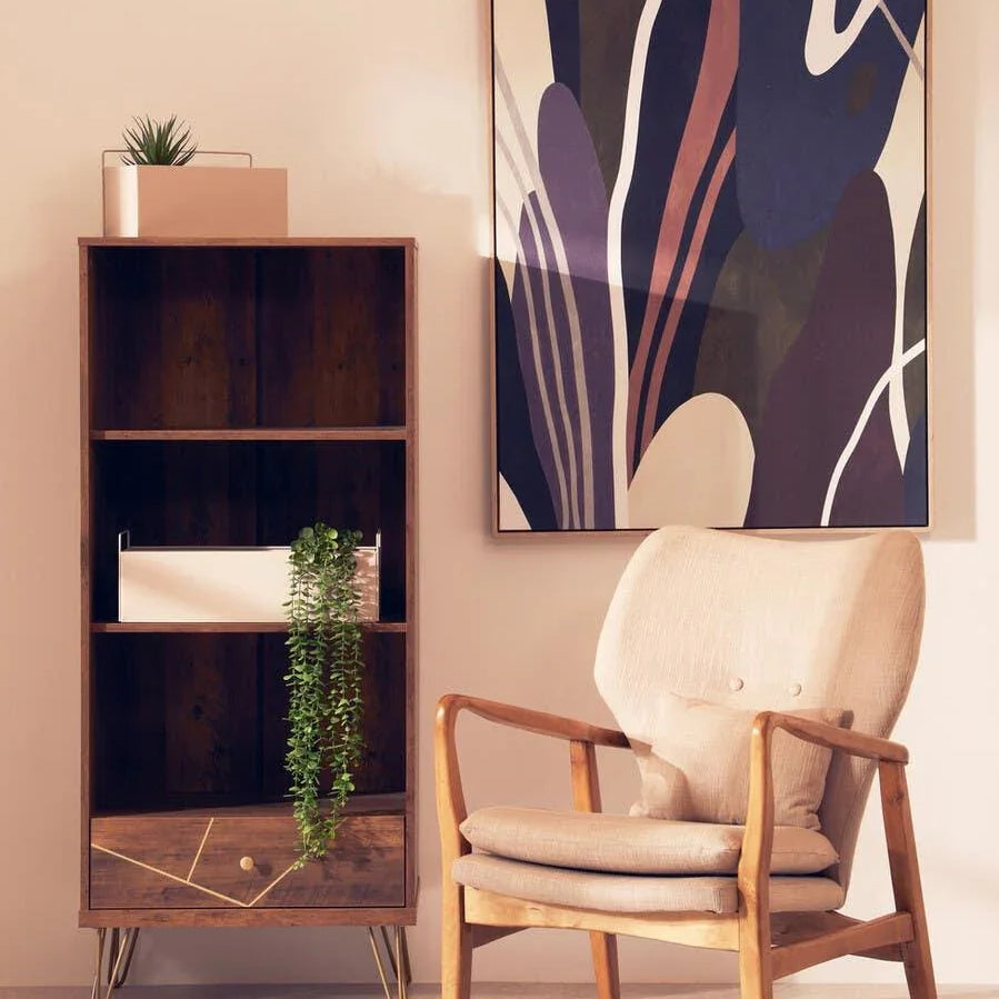 Wooden armchair with cream cushions beside a modern bookcase and abstract wall art
