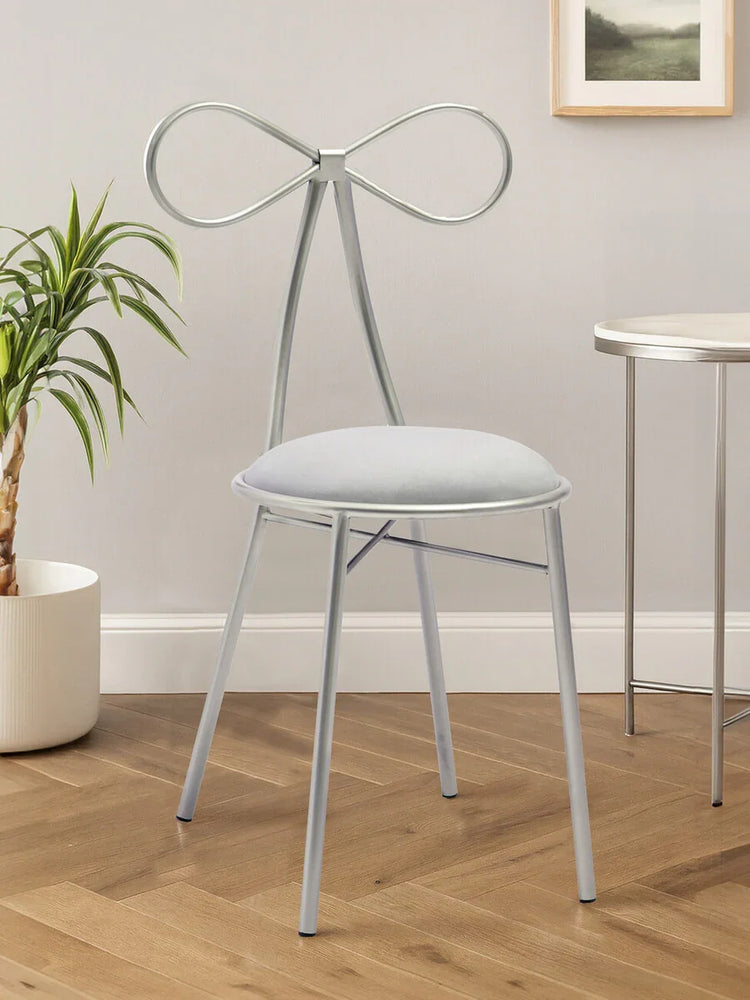 Silver metal dining chair with bow-shaped back and cushioned seat on wooden floor