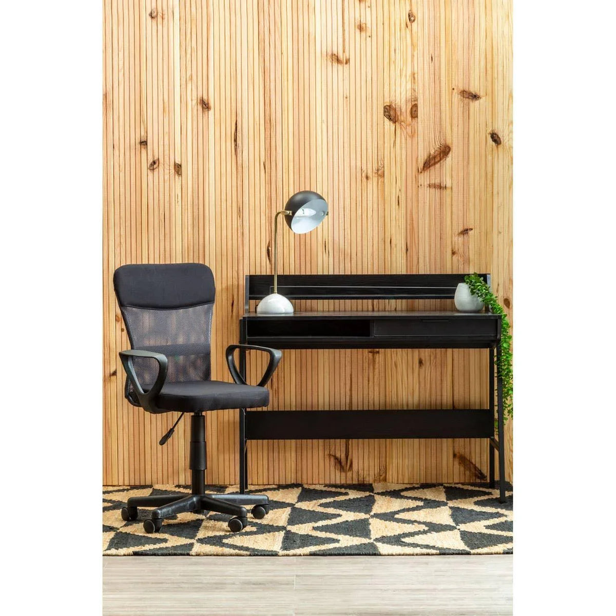 Black mesh office chair and modern black desk with lamp against wood panel wall