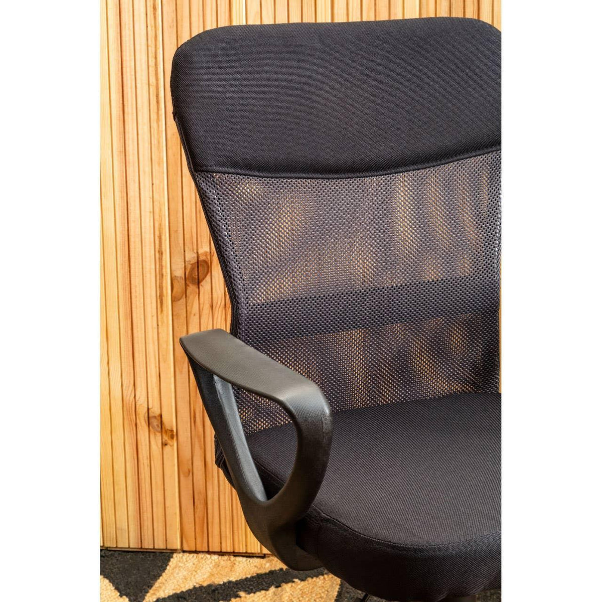 Black mesh office chair with armrest against wooden panel wall