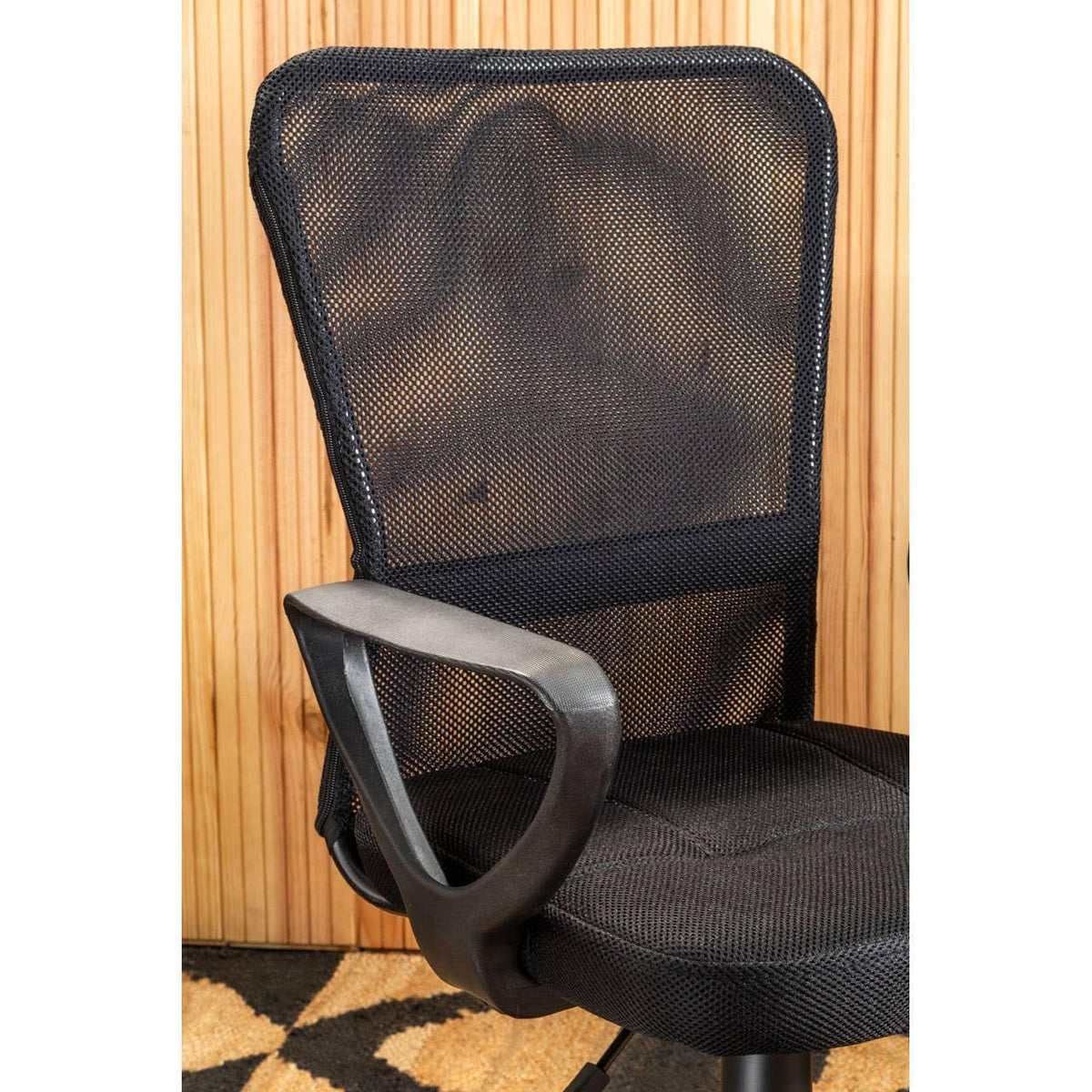 Black mesh office chair with armrests against wood panel wall