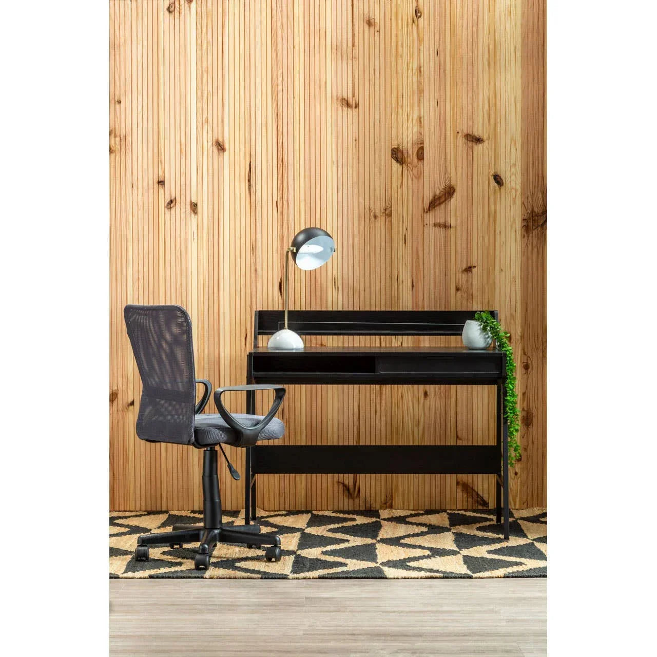 Black home office desk with mesh chair, lamp, and decor against wood panel wall