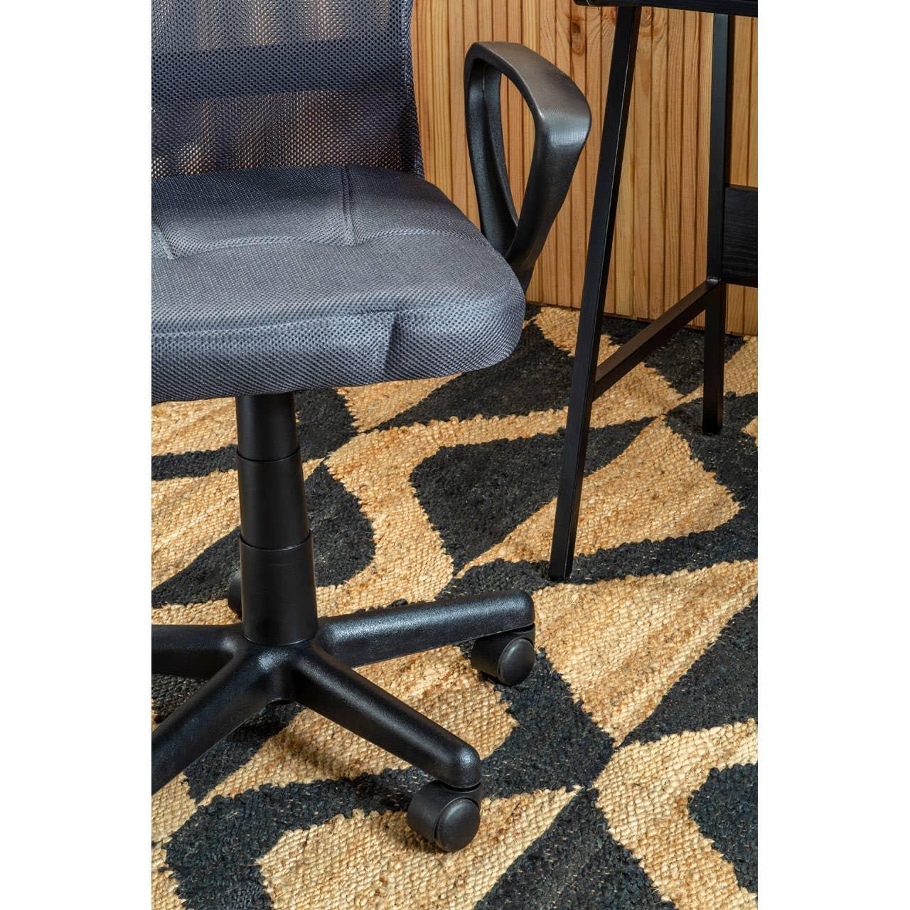 Black mesh office chair with castors beside wooden desk on patterned rug