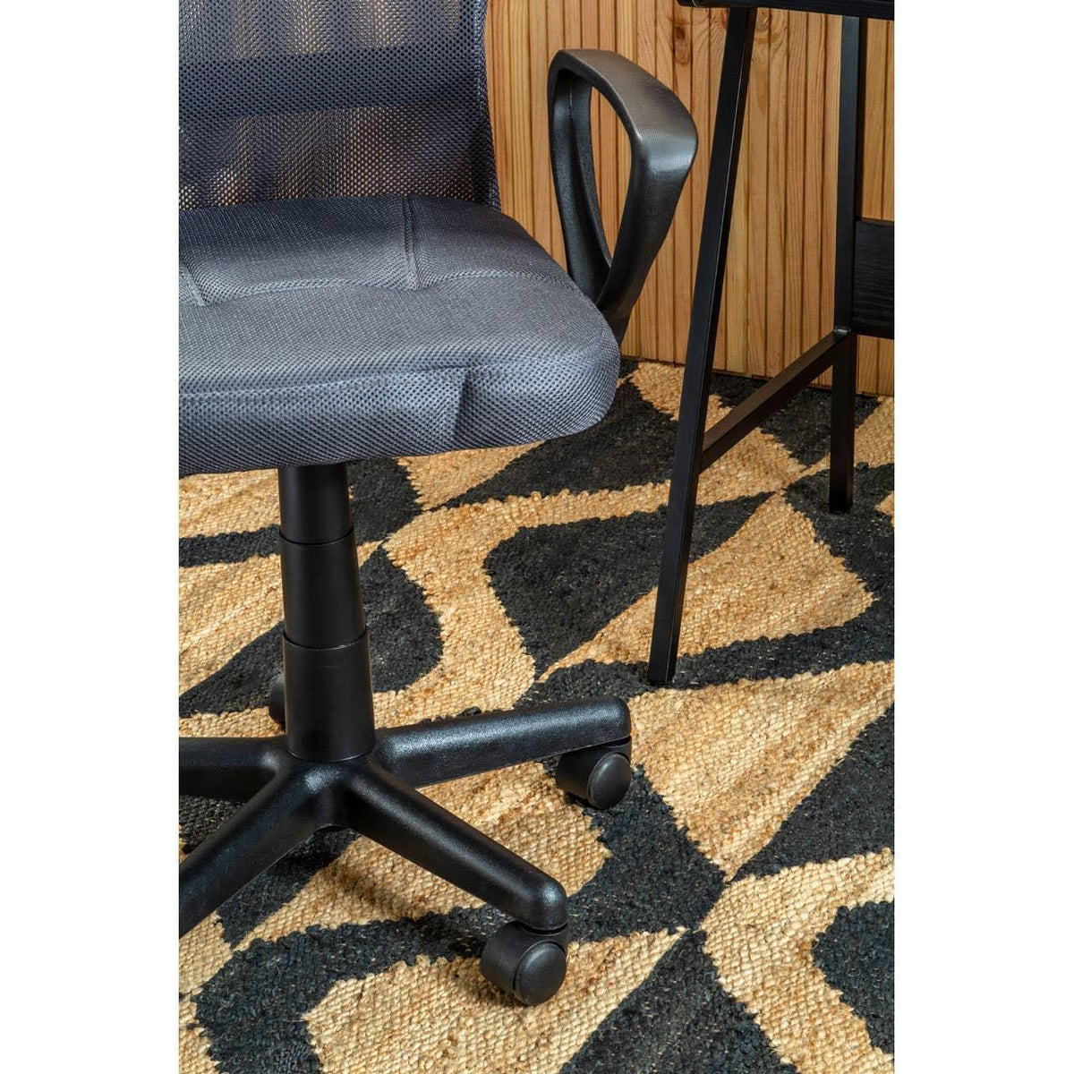 Black mesh office chair with castors beside wooden desk on patterned rug