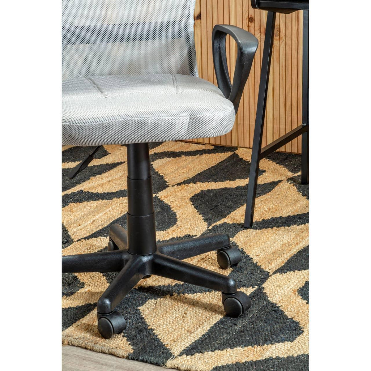 Grey mesh office chair with black plastic armrest and wheeled base on patterned rug