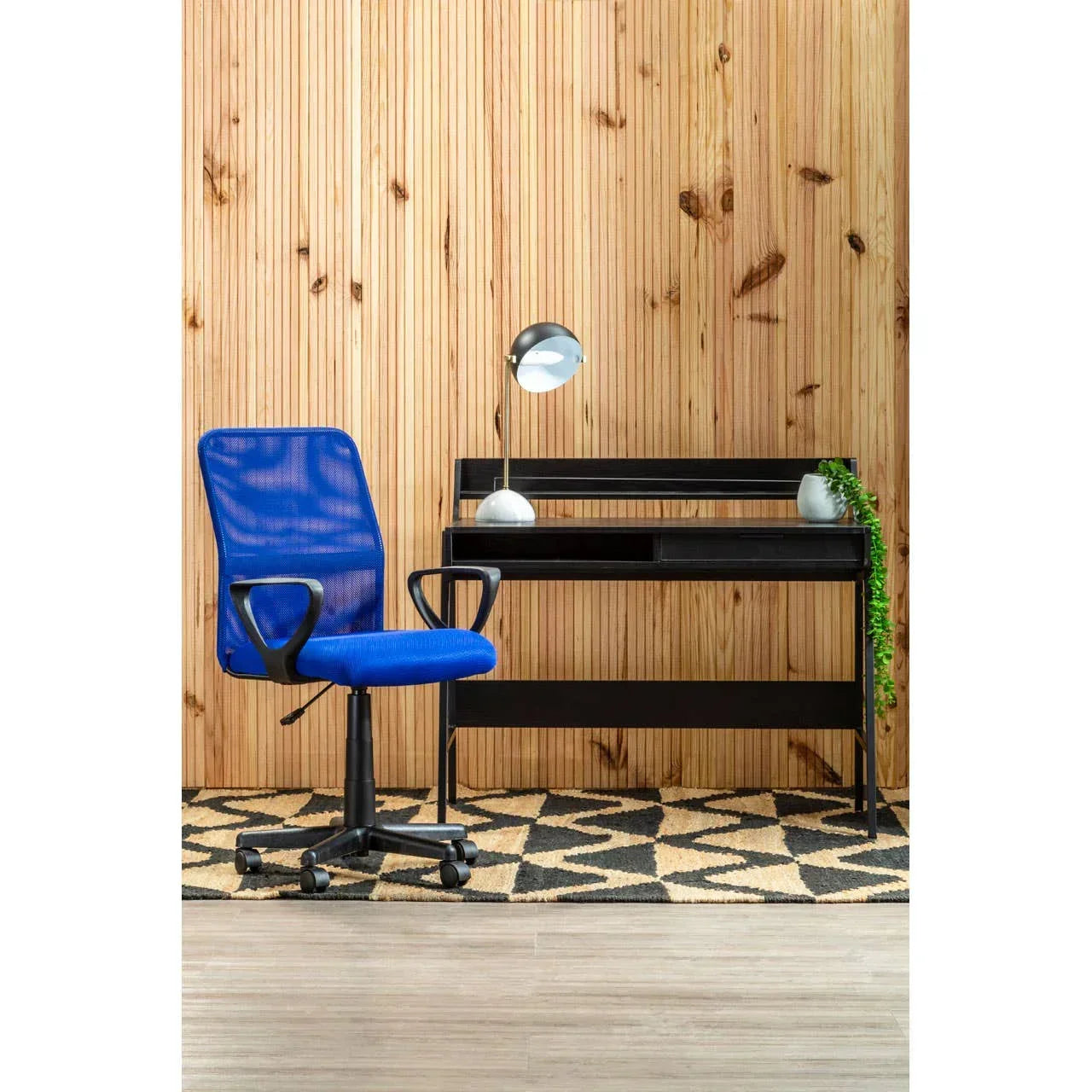 Blue mesh office chair with black computer desk and lamp on geometric rug