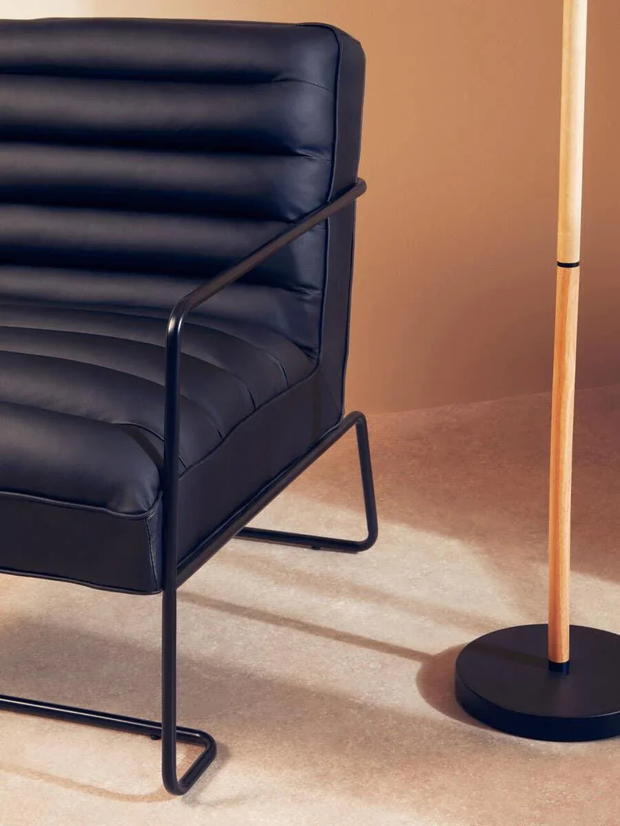 Black leather accent chair with black metal frame beside wooden floor lamp base