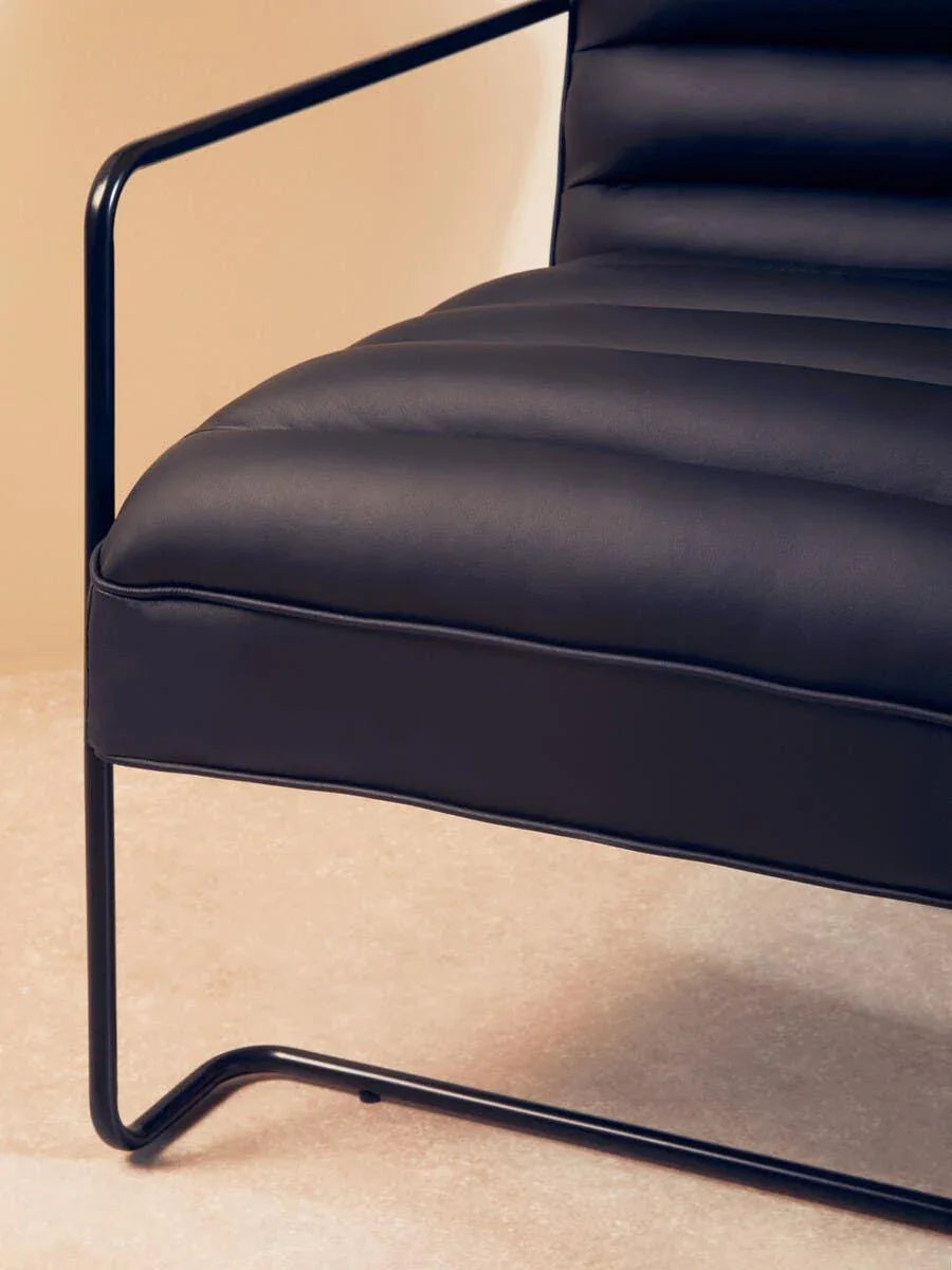 Black leather accent chair with metal frame and stitched cushioning, close-up side view