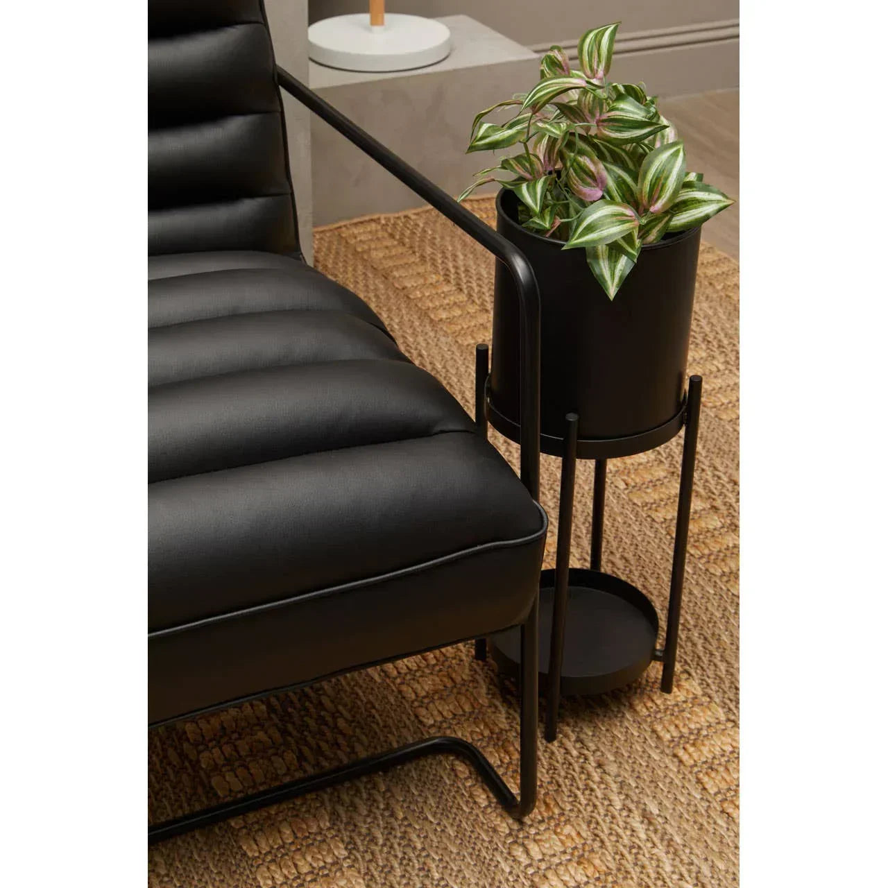Black leather armchair with metal frame next to a black plant stand on woven rug