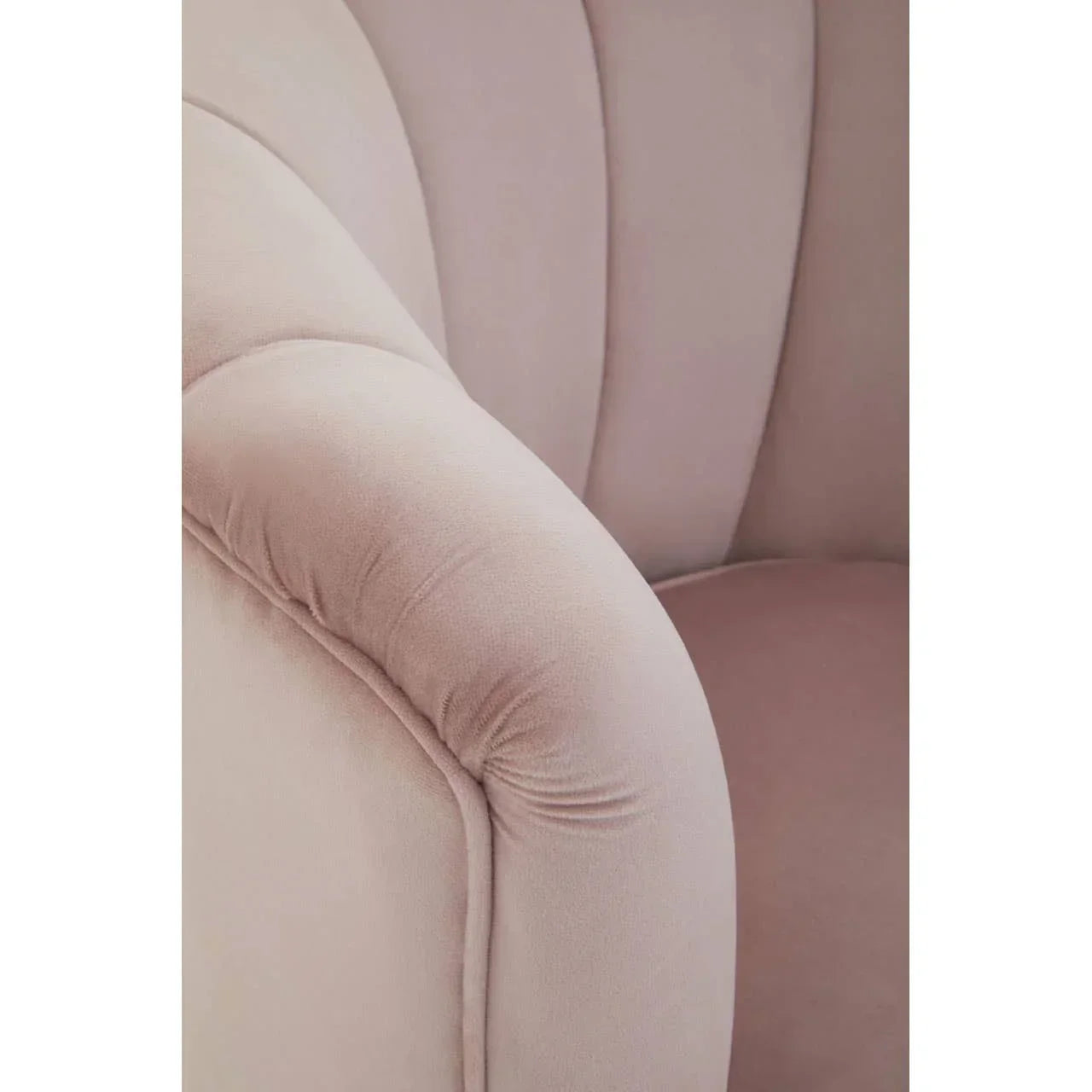 Close-up of blush pink velvet armchair with curved arm and stitched detailing