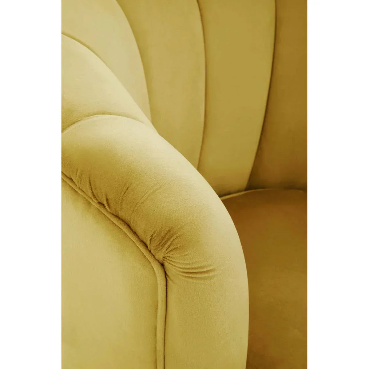 Close view of mustard yellow velvet armchair showing curved arm and stitched detail