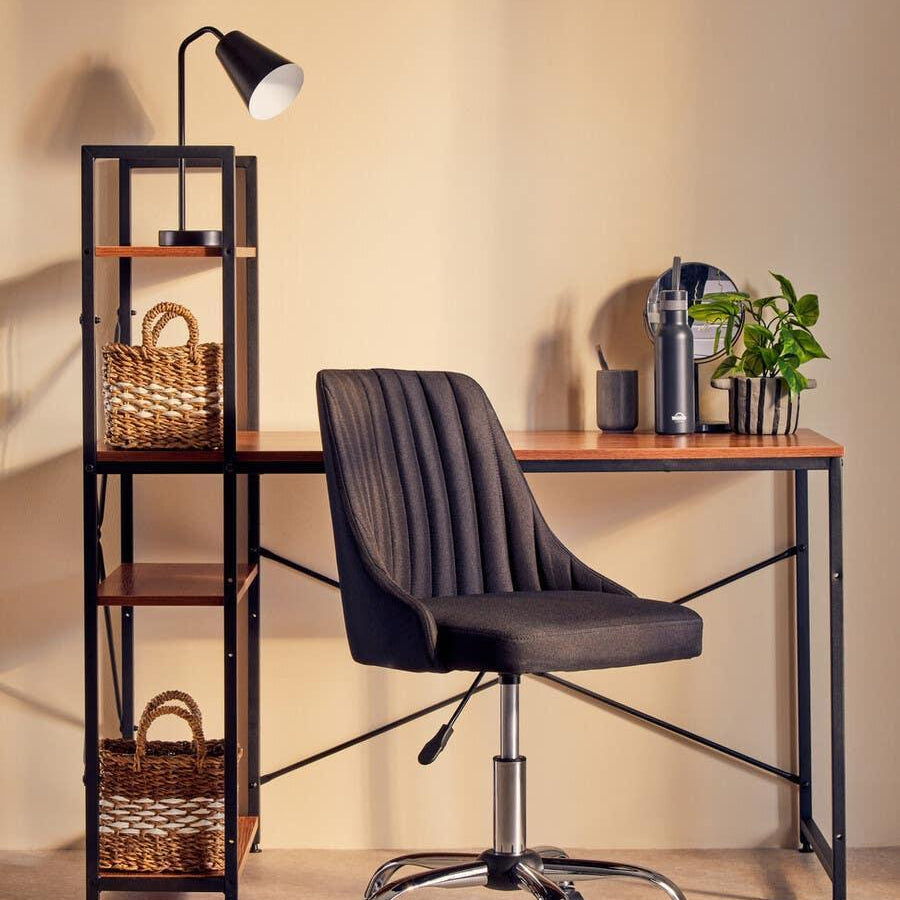 Contemporary black office chair at wood desk with shelving unit and desk lamp