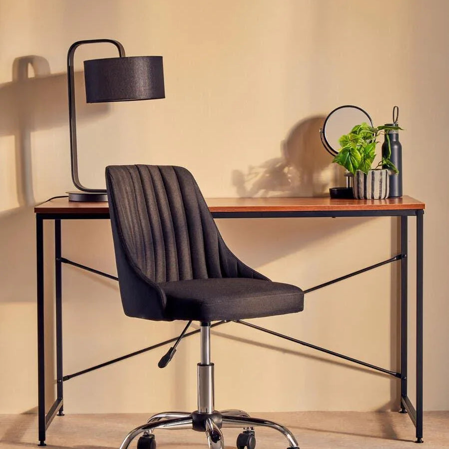 Black office chair with chrome base at wooden desk with lamp and plant