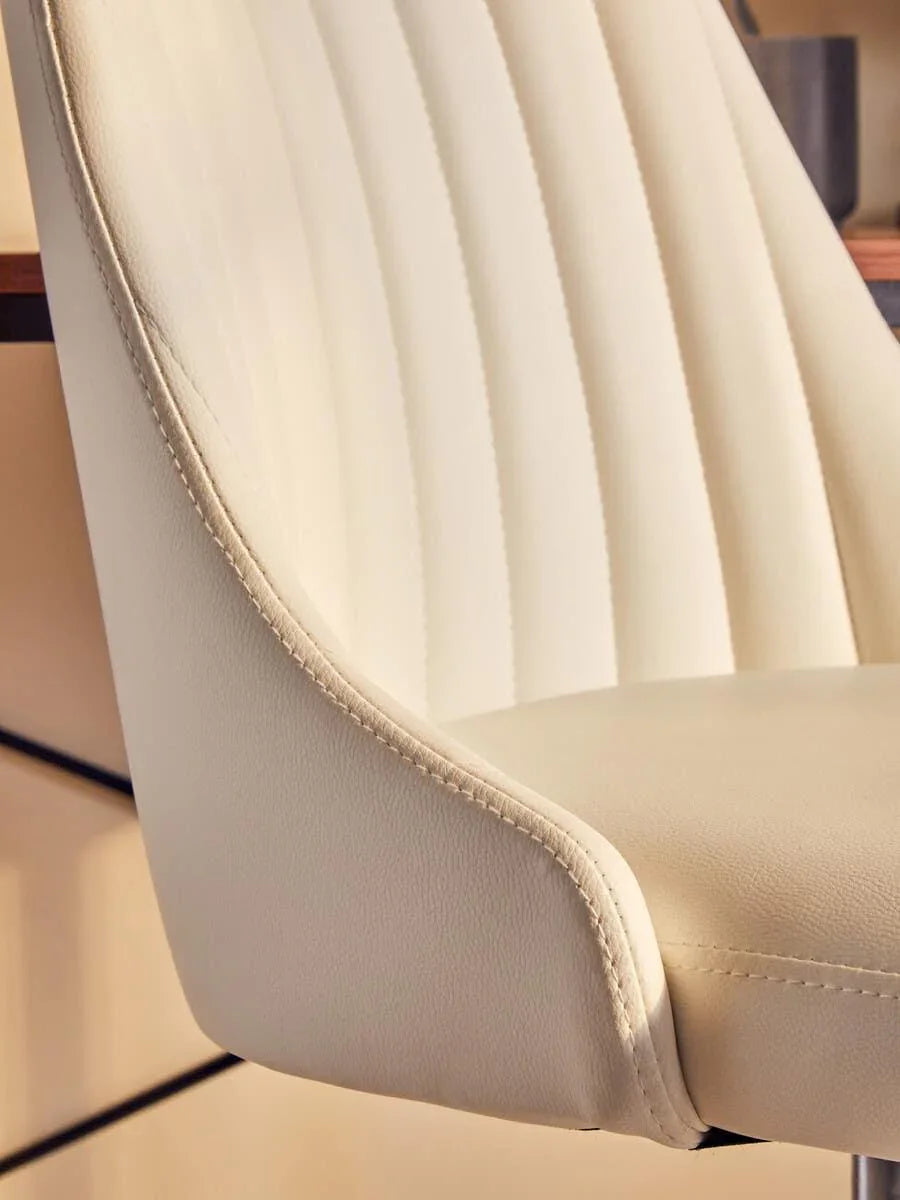 Cream faux leather dining chair with vertical stitching and padded seat, side view