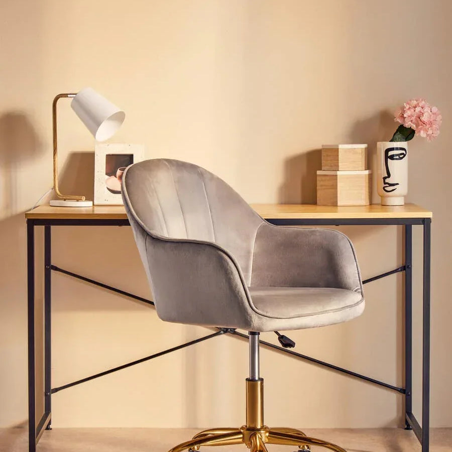 Grey velvet office chair with gold base at minimalist desk with lamp and vase