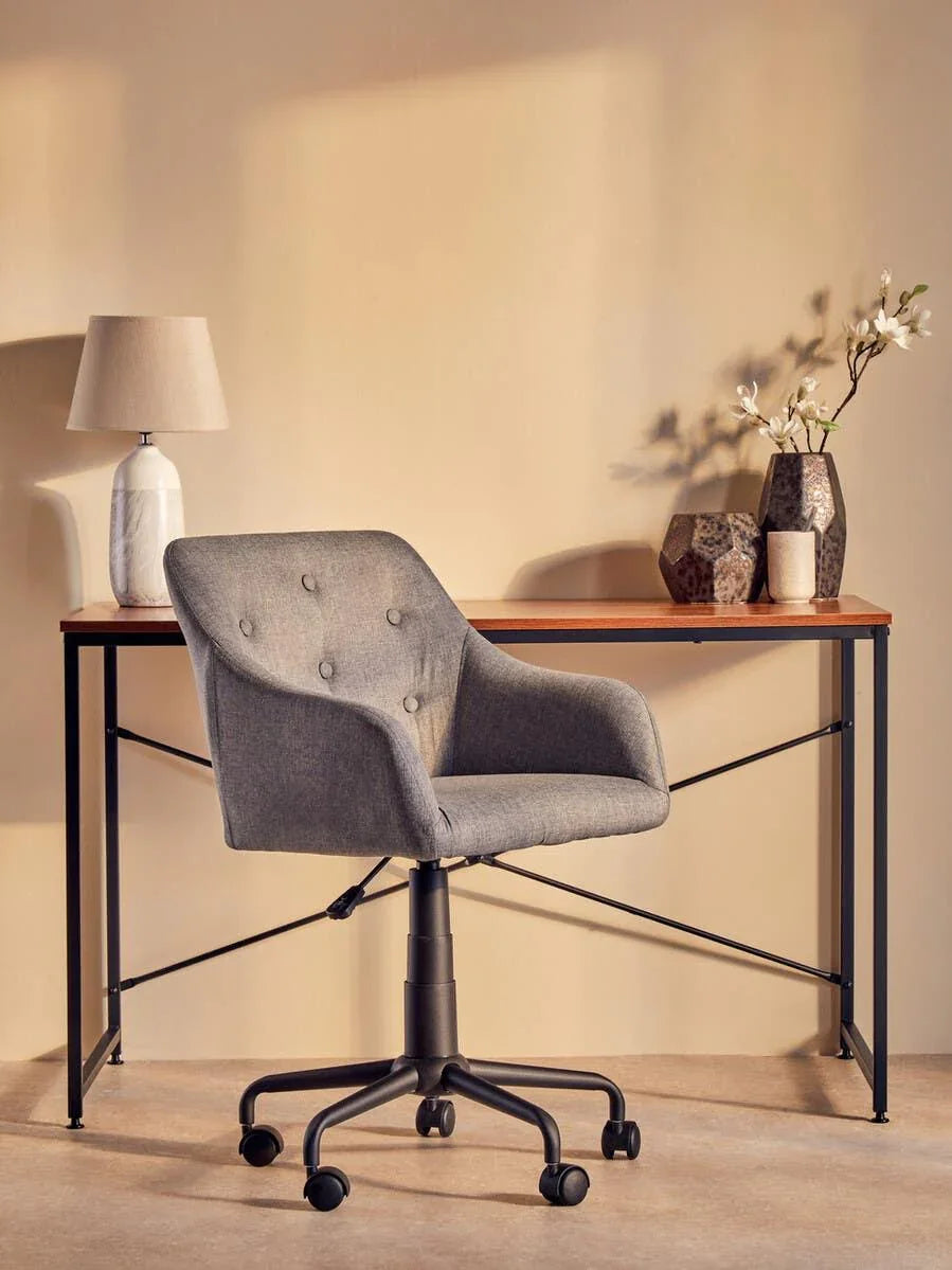 Grey fabric office chair with casters at wooden desk, lamp and vases in home workspace
