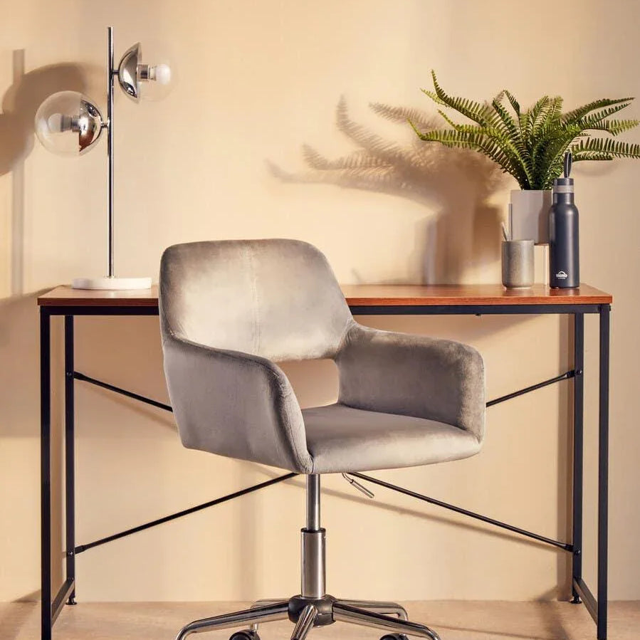 Grey office chair with chrome base at modern wooden desk, desk lamp and plant decor