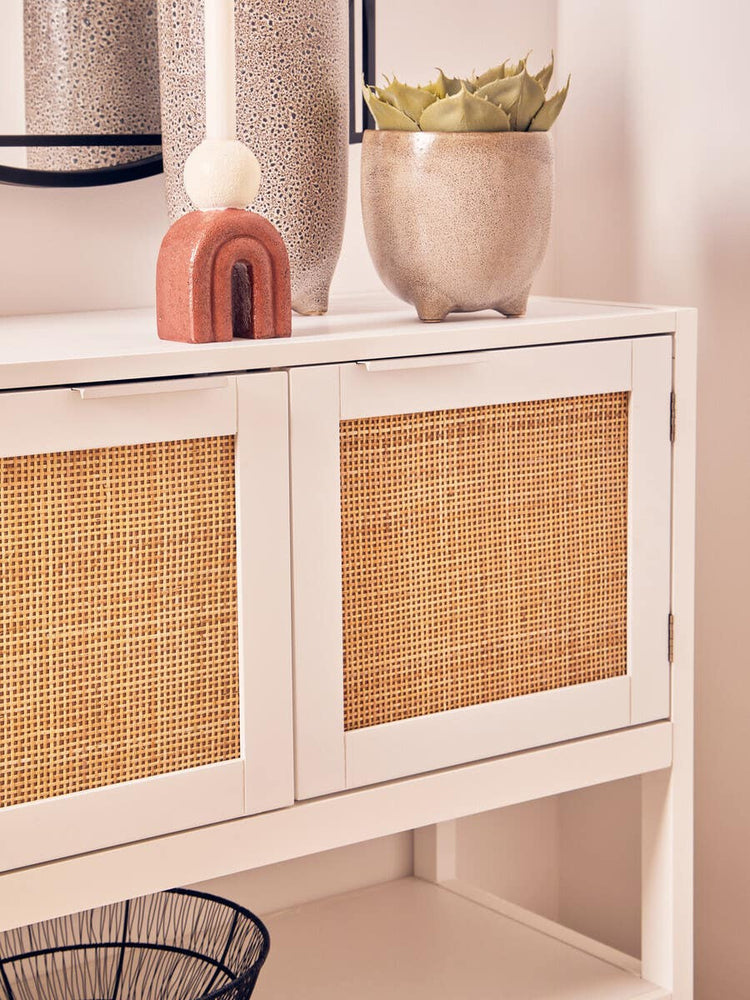 White wood side cabinet featuring two rattan front drawers, styled with a decorative vase and a small plant on top, against a neutral wall backdrop