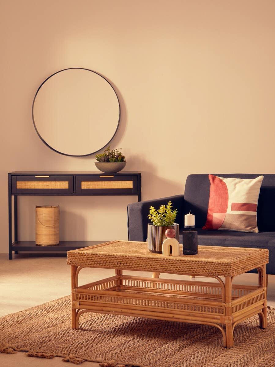 Rattan coffee table on woven rug with navy sofa and round mirror in living room setting