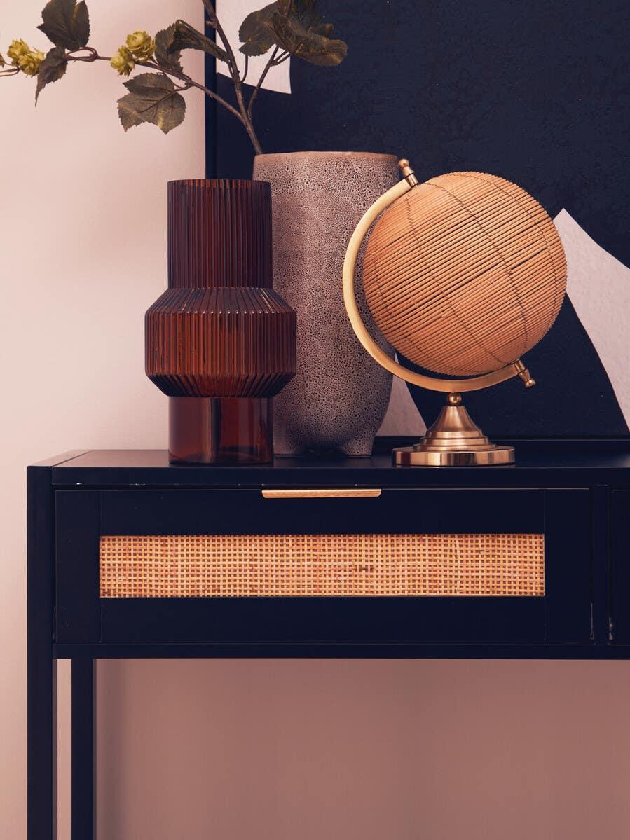 Black console table with rattan drawer, decorative globe, brown vase, and plant arrangement
