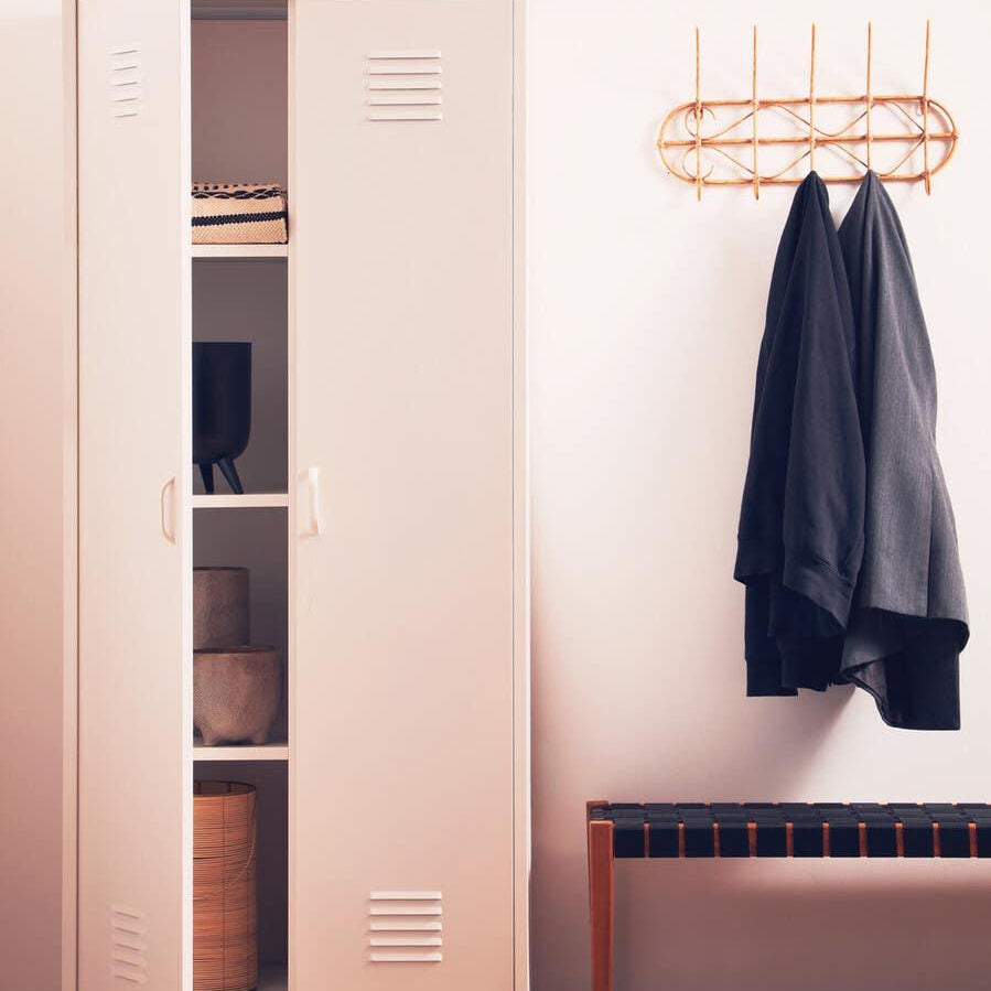 White metal storage cabinet with open doors beside bench and wall coat rack in hallway