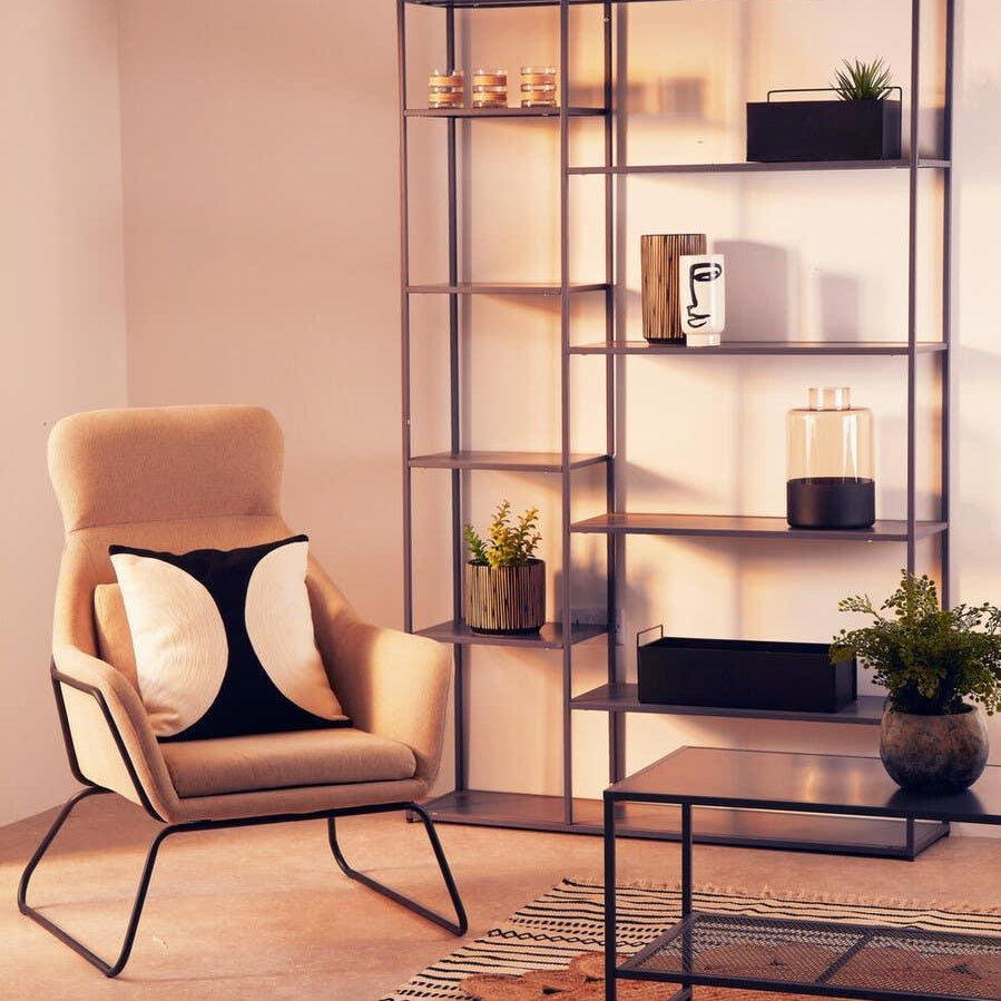Modern beige accent chair with cushion beside black metal shelving unit and coffee table