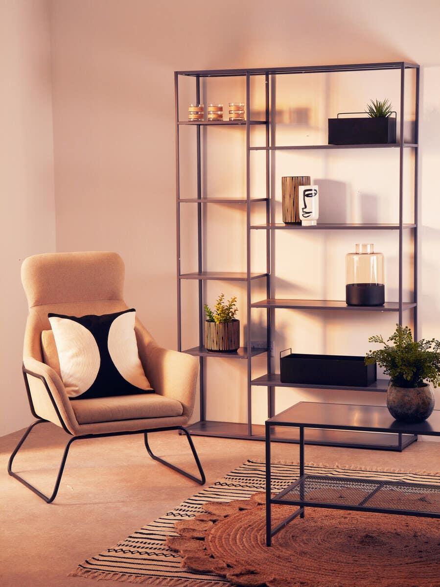 Modern beige accent chair with cushion beside black metal shelving unit and coffee table