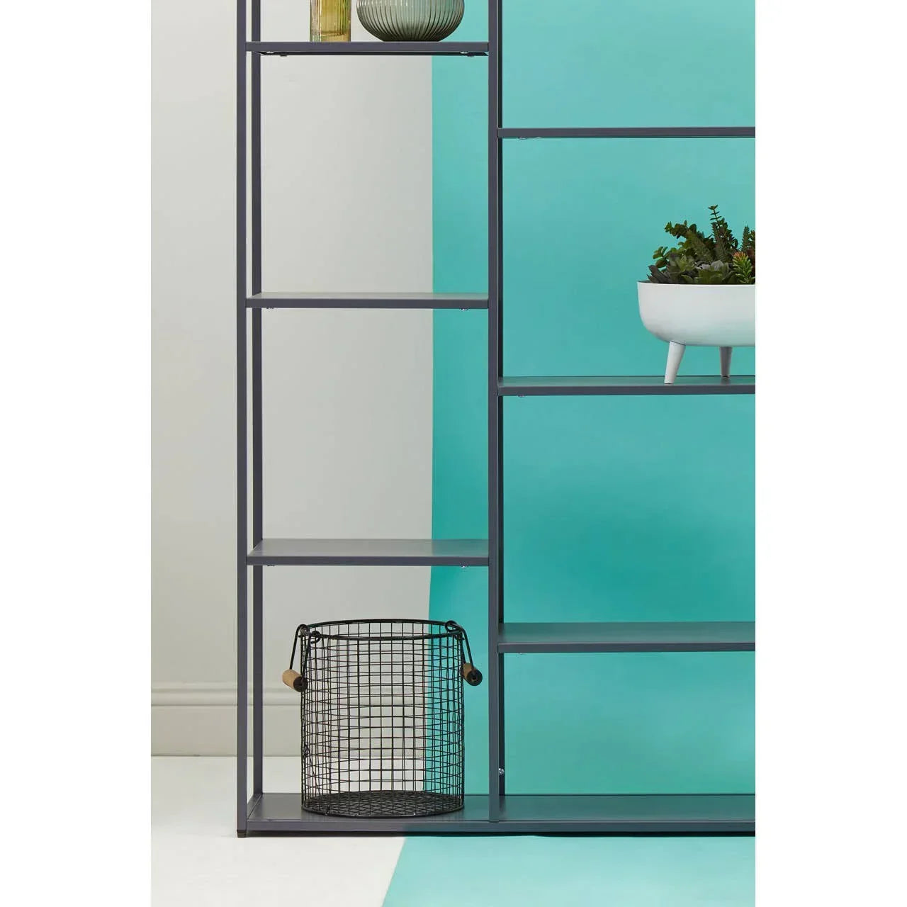 Black metal shelving unit with decorative accessories and wire storage basket against blue wall