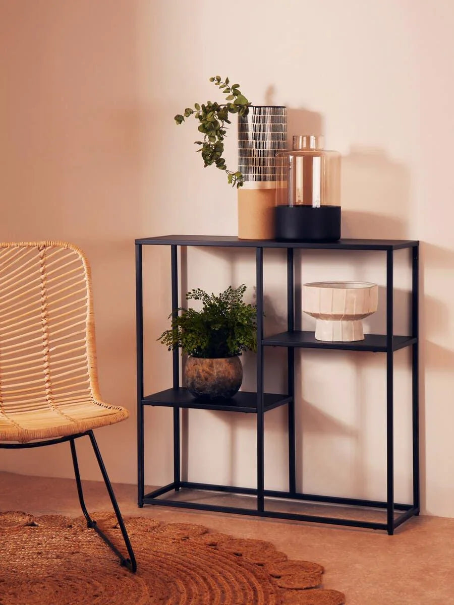 Black metal console table with plants and decorative vases, wicker chair on the side