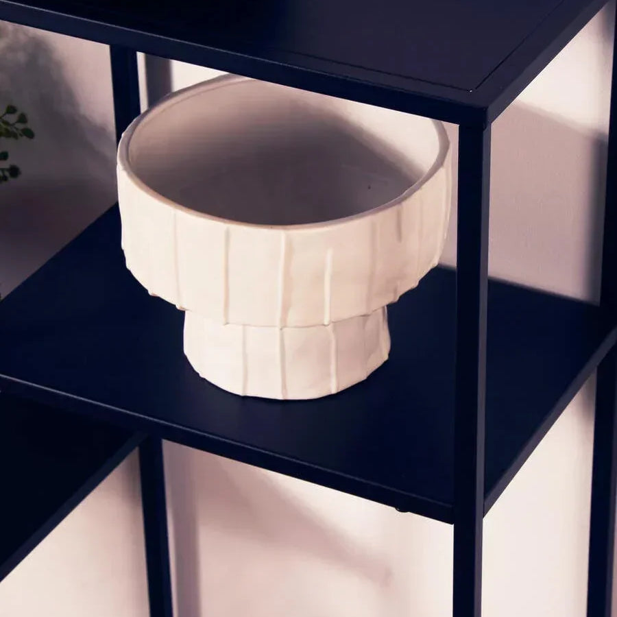 White ceramic vase on black metal shelving unit against light wall