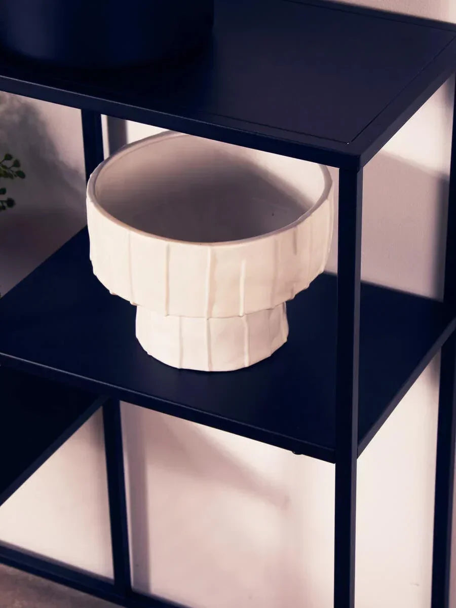 White ceramic vase on black metal shelving unit against light wall