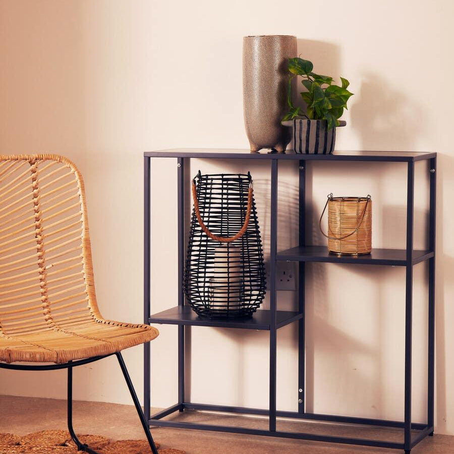 Black metal console table with decorative vases, lanterns, and indoor plant beside rattan chair