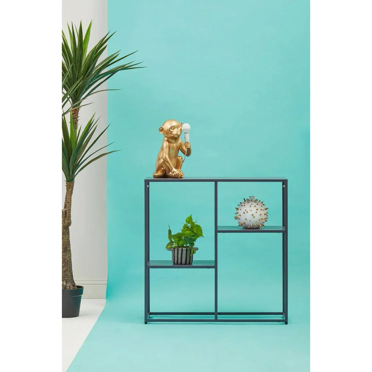 Black metal shelving unit with potted plant, gold monkey lamp, decorative vase and palm plant
