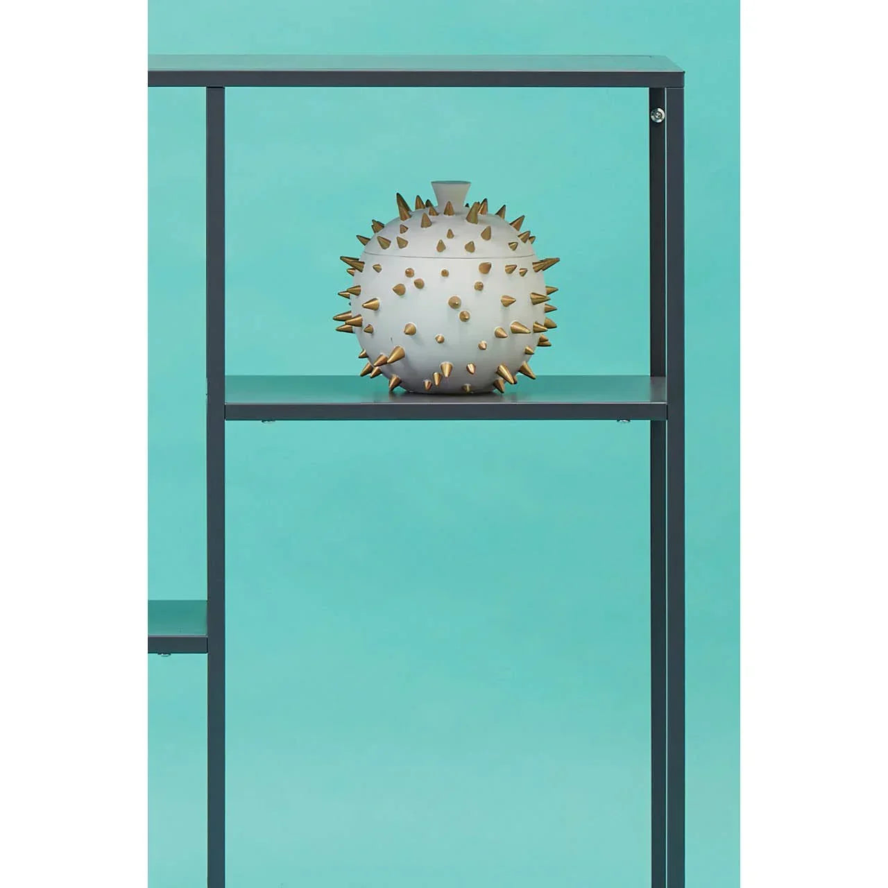 White ceramic vase with gold spikes on black shelving unit against turquoise background