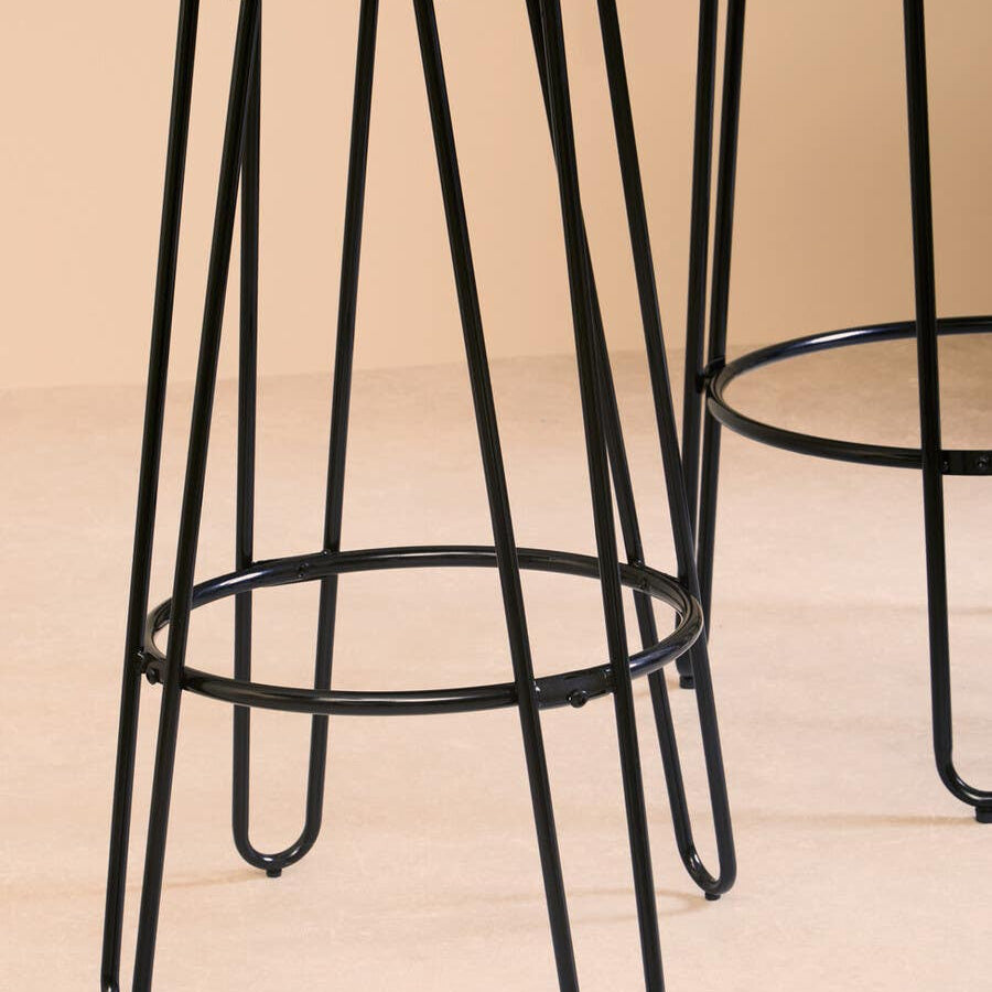 A black metal bar stool with a round seat and slender legs, featuring a minimalist design. The stool is positioned next to a tall bar table, showcasing the set's modern aesthetic against a neutral background