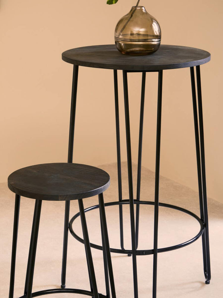 A modern three-piece bar table and stool set featuring a round black tabletop supported by slender black metal legs, with a matching round stool positioned beside it. A decorative vase sits on the table, set against a soft beige background