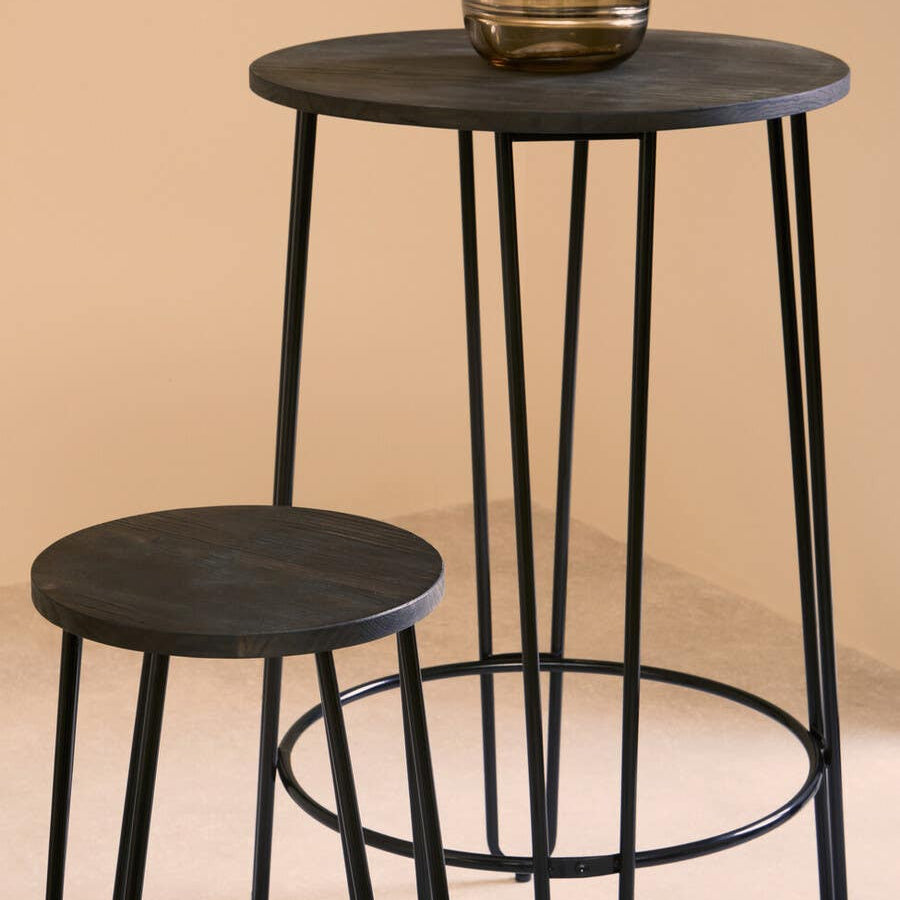 A modern three-piece bar table and stool set featuring a round black tabletop supported by slender black metal legs, with a matching round stool positioned beside it. A decorative vase sits on the table, set against a soft beige background